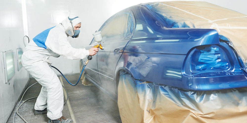 Featured image for Auto Body Technician Jobs at Byrne Auto depicting man in work suit painting a car.