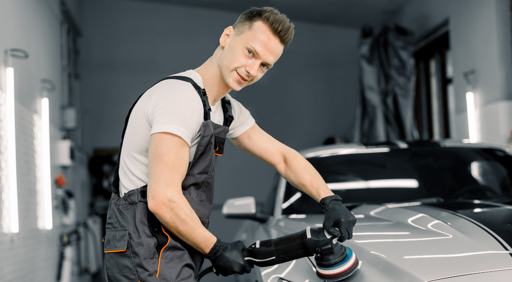 Featured image for Auto Detailer Jobs at Byrne Auto depicting man smiling at camera while buffing a car.